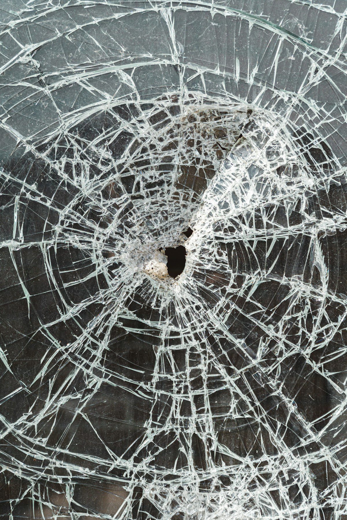 A cracked glass window with a hole from impact, illustrating the need for shatterproof security window film