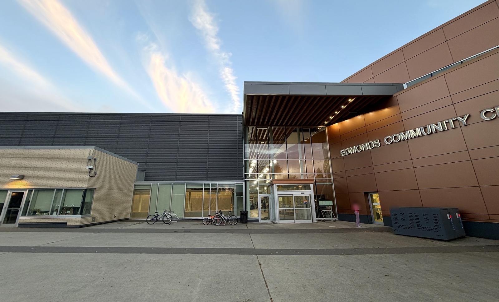 Site-visit exterior view of the community centre entrance; pedestrian faces are blurred.